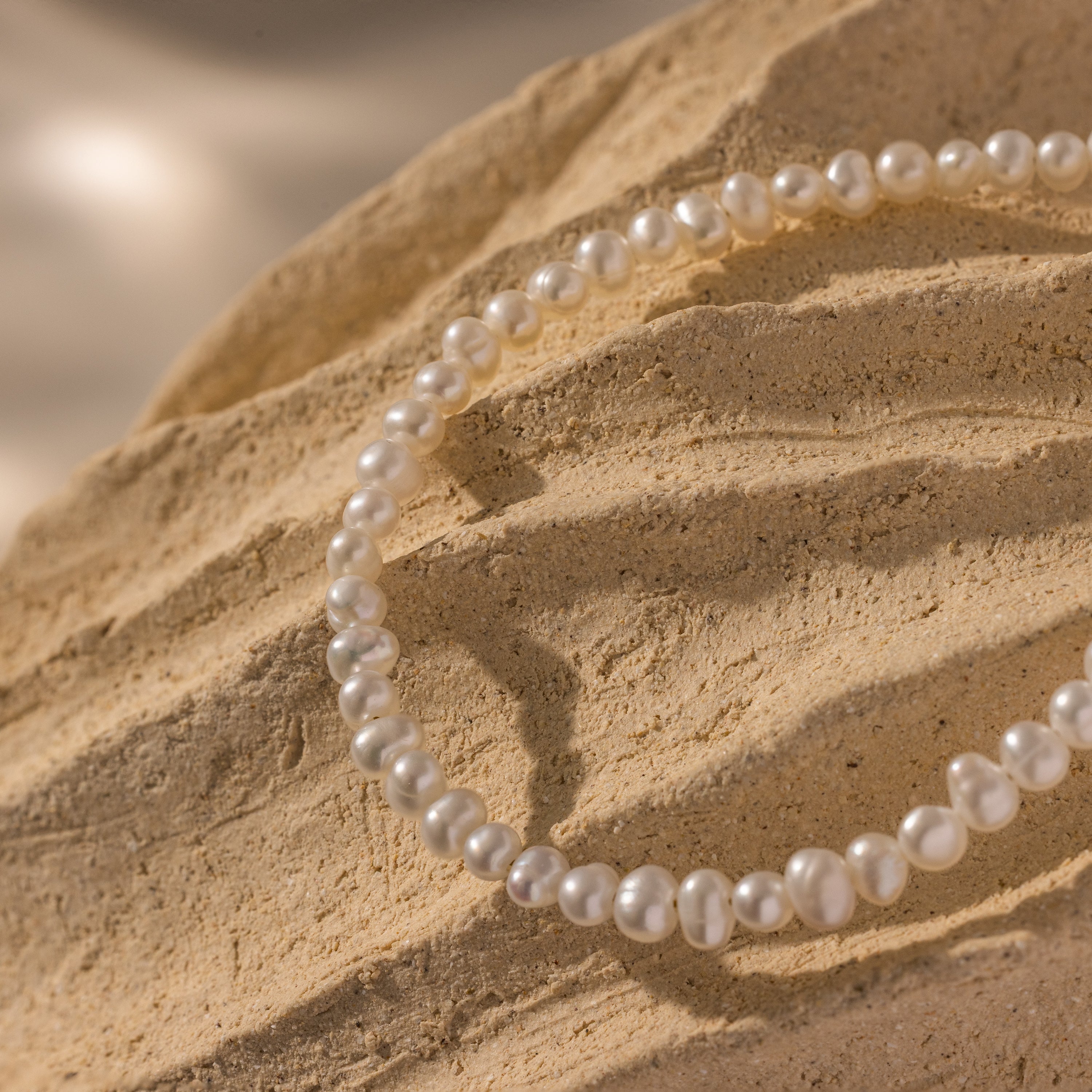 The Venus Pearl Bracelet rests on a textured beige rock, illuminated by soft natural light to highlight the elegance of its freshwater pearls.
