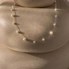The Floating Pearl Necklace, featuring delicate freshwater pearls, is displayed on smooth beige rounded stones, casting soft shadows.