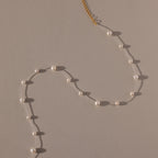 The Floating Pearl Necklace, featuring delicate freshwater pearls and a gold clasp, is arranged in a graceful curve on a beige surface.