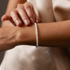 A person wearing the Venus Pearl Bracelet—an elegant freshwater pearl accessory—gently touches it on their wrist.