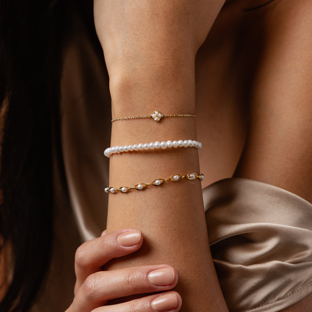 A woman in a satin dress rests her hand on her arm, wearing three delicate bracelets, including the Venus Pearl Bracelet.