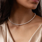 A woman wears the Venus Pearl Necklace, a single-strand freshwater pearl piece, paired with a champagne satin top, showcasing timeless jewelry elegance.
