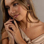 Woman with long hair smiles softly while wearing the Floating Pearl Necklace and a satin off-shoulder top.