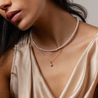 Woman in a silky beige top layers the Venus Pearl Necklace with a gold pendant, showcasing timeless jewelry elegance.