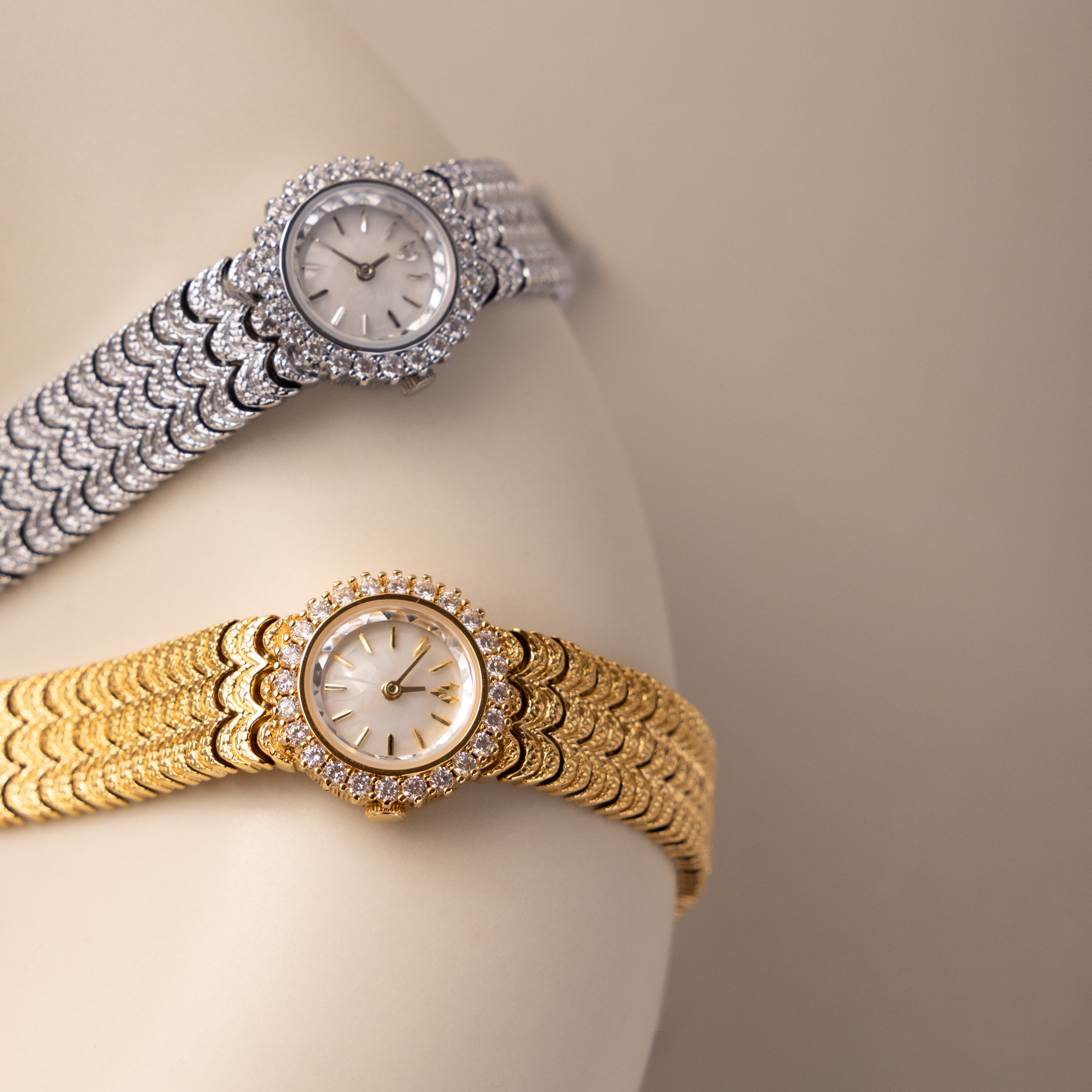 Two Pave Scalloped Timepieces, one gold and one silver with diamond-studded faces and pavé bezels, are paired with chic scallop-link bracelets and displayed against a neutral backdrop.