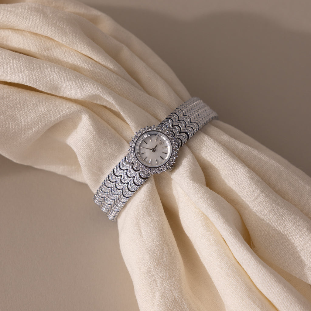 A Pave Scalloped Timepiece in White Gold with a pavé bezel is displayed on cream-colored, folded fabric.