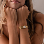 A woman rests her chin on her fists, displaying the Brick Link Timepiece with its bold brick-link bracelet, long hair draping over her shoulders against a neutral backdrop.