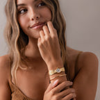 Woman with wavy hair, smiling and looking to the side, wears the Brick Link Timepiece—a sculptural watch with a bold brick-link bracelet.