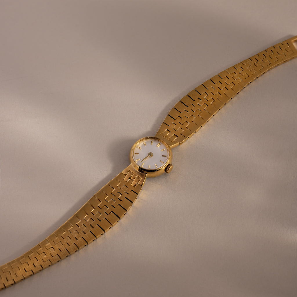 The Brick Link Timepiece, featuring a white face and bold brick-link bracelet, is displayed diagonally on a light beige surface.