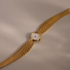 The Brick Link Timepiece, featuring a white face and bold brick-link bracelet, is displayed diagonally on a light beige surface.