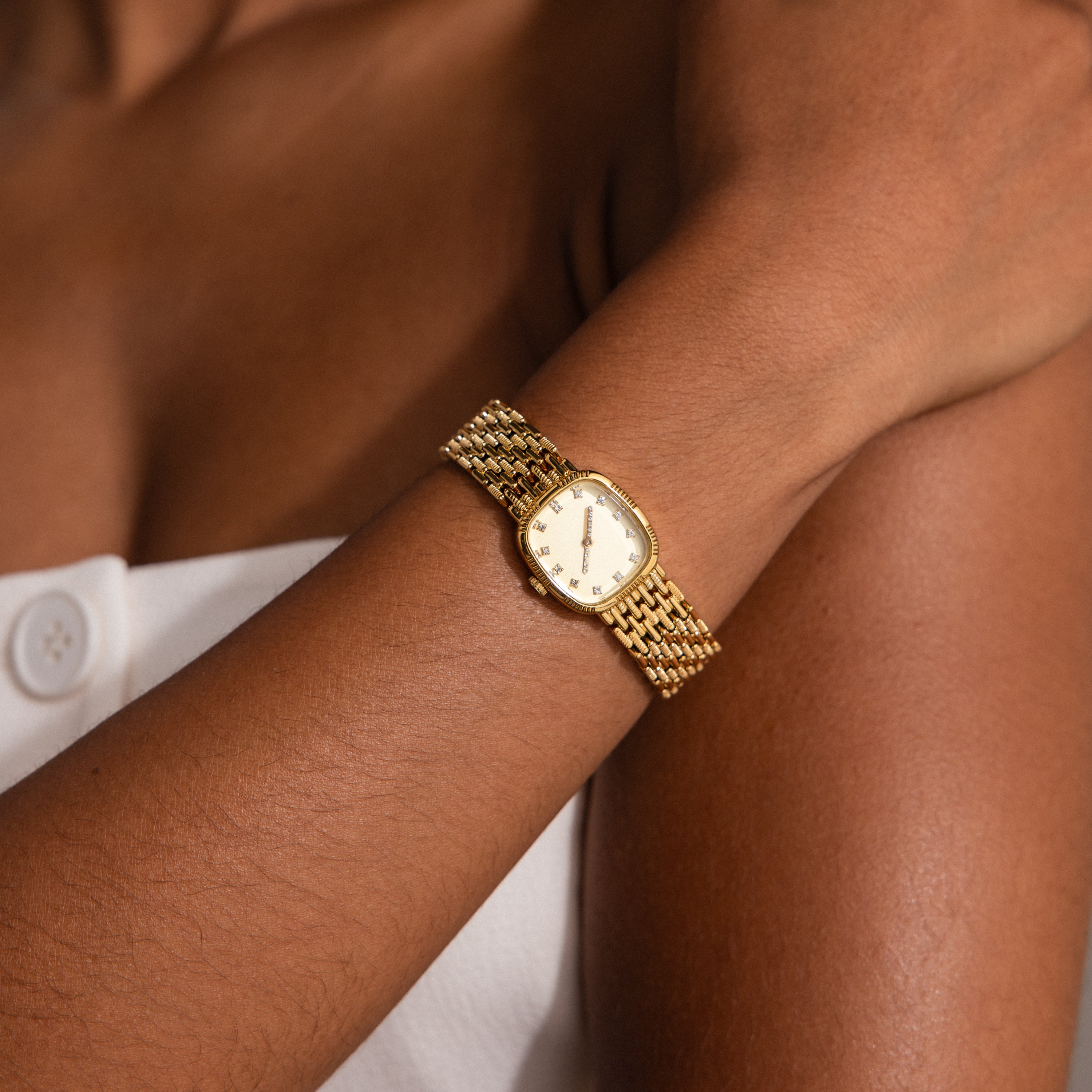 A person wearing the Pave Woven Timepiece in gold with a white sleeveless buttoned top.
