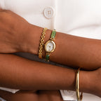 Close-up of a wrist adorned with the Jade Band Timepiece, featuring a gold case, green accents, and a minimalist oval dial, paired stylishly with a gold bracelet and jade band.
