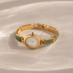 The Jade Band Timepiece features a minimalist oval dial, white face, and green jade link bracelet, displayed on a light textured surface.