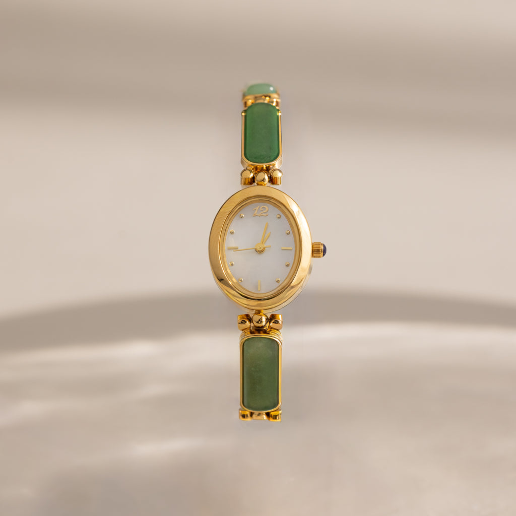 Jade Band Timepiece featuring a minimalist oval gold dial and an elegant green jade band, displayed on a neutral background.