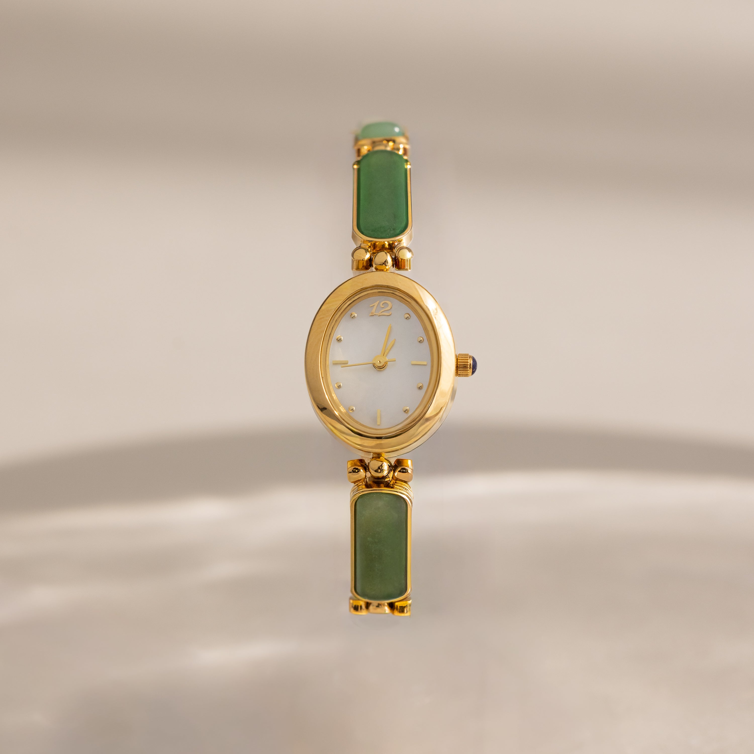 Jade Band Timepiece featuring a minimalist oval gold dial and an elegant green jade band, displayed on a neutral background.