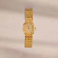 The Pave Woven Timepiece features a gold rectangular face, diamond hour markers, and pavé accents on a woven bracelet, elegantly displayed against a neutral background.