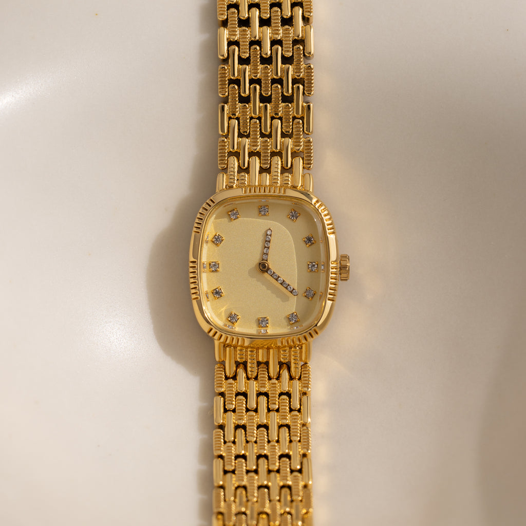 The Pave Woven Timepiece is a gold wristwatch with a rectangular face, diamond hour markers, and pavé accents on its sophisticated gold metal band.