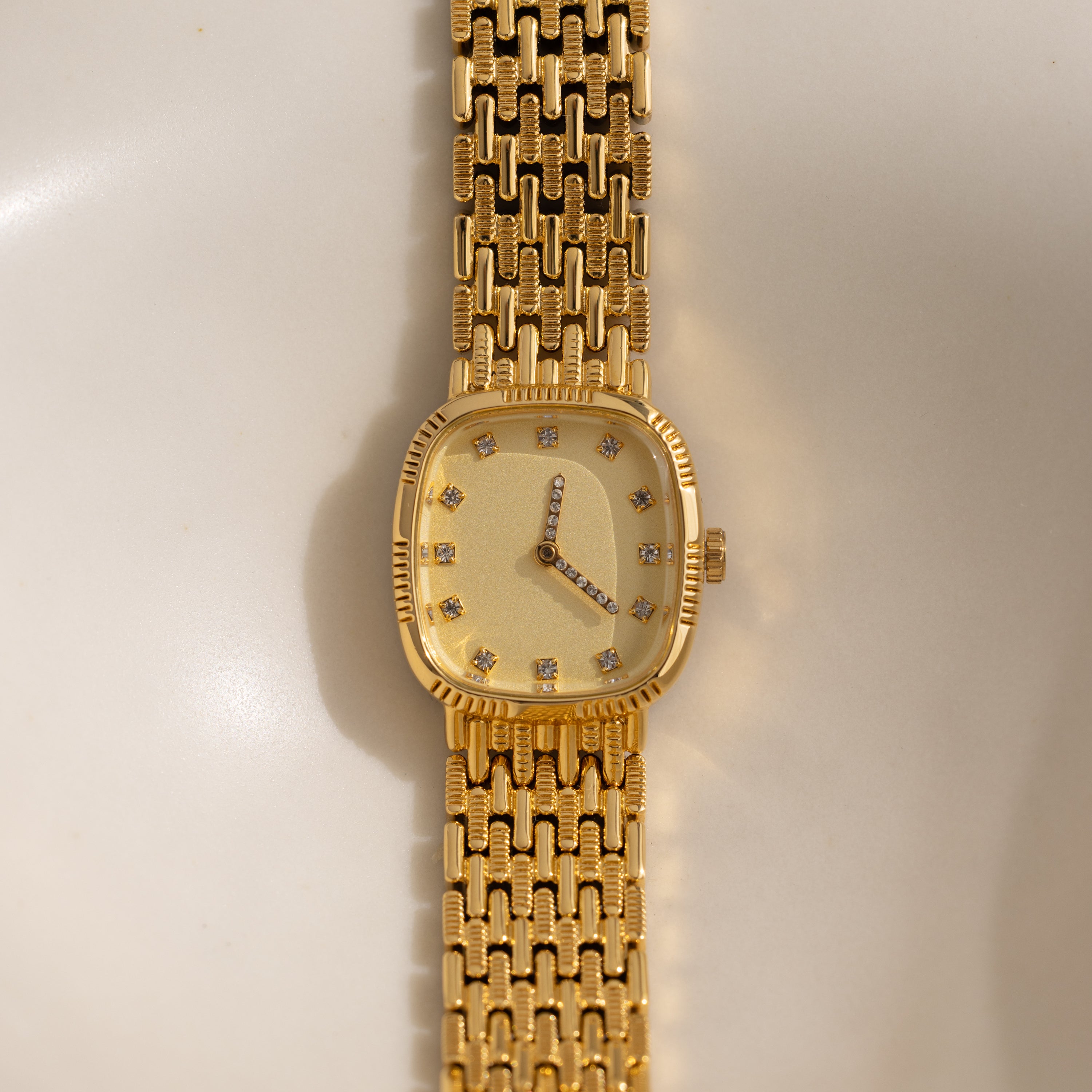 The Pave Woven Timepiece is a gold wristwatch with a rectangular face, diamond hour markers, and pavé accents on its sophisticated gold metal band.