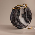 The Onyx Marble Jewelry Dish holds gold and pearl necklaces draped over its surface, with a gold ring placed nearby on a beige background.