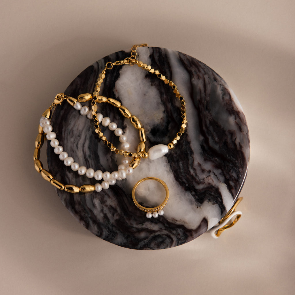 Gold and pearl jewelry displayed on a Marble Jewelry Dish featuring a black and white marbled surface.