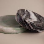 The Marble Jewelry Dish set includes two round dishes—one green and one with black and white swirls—resting on a beige background, perfect as elegant holders for your favorite jewelry pieces.