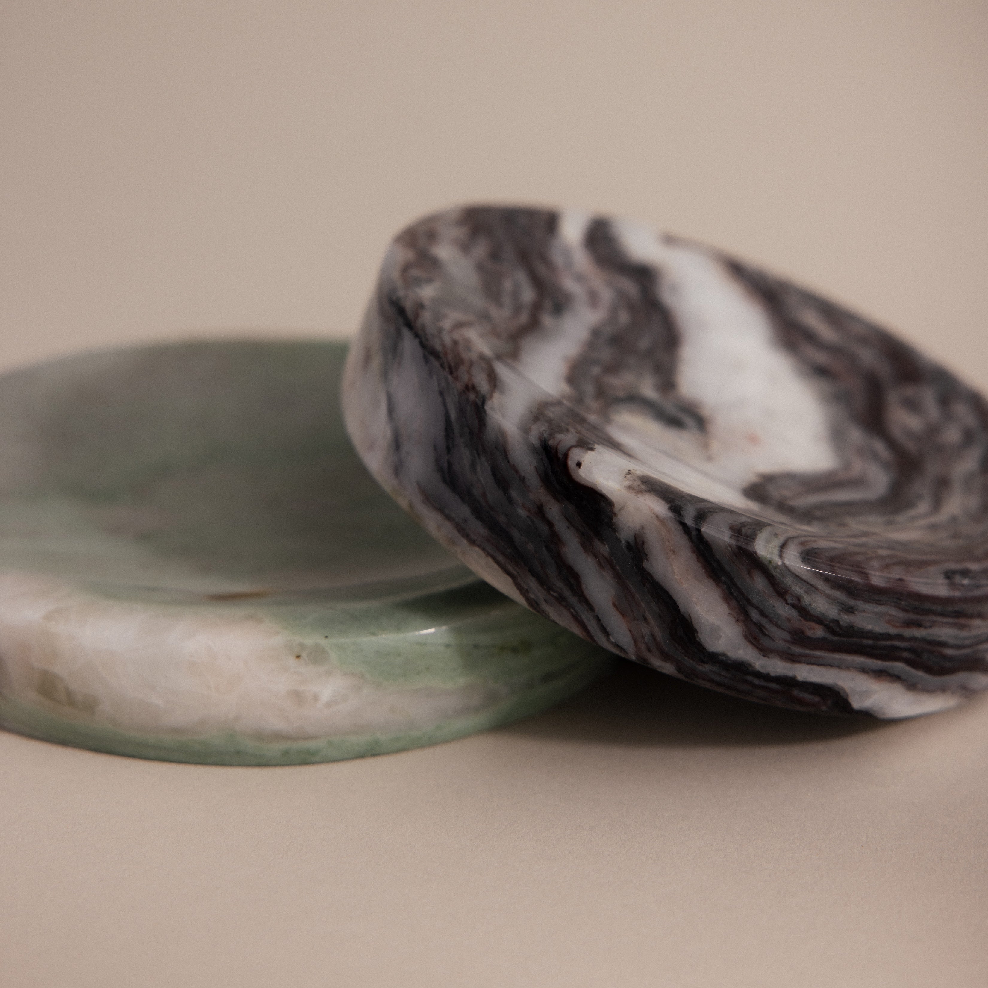 The Marble Jewelry Dish set includes two round dishes—one green and one with black and white swirls—resting on a beige background, perfect as elegant holders for your favorite jewelry pieces.