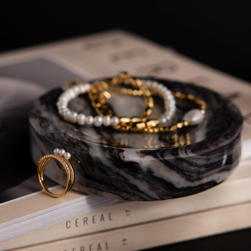 A Marble Jewelry Dish holding gold and pearl jewelry is displayed atop stacked books.