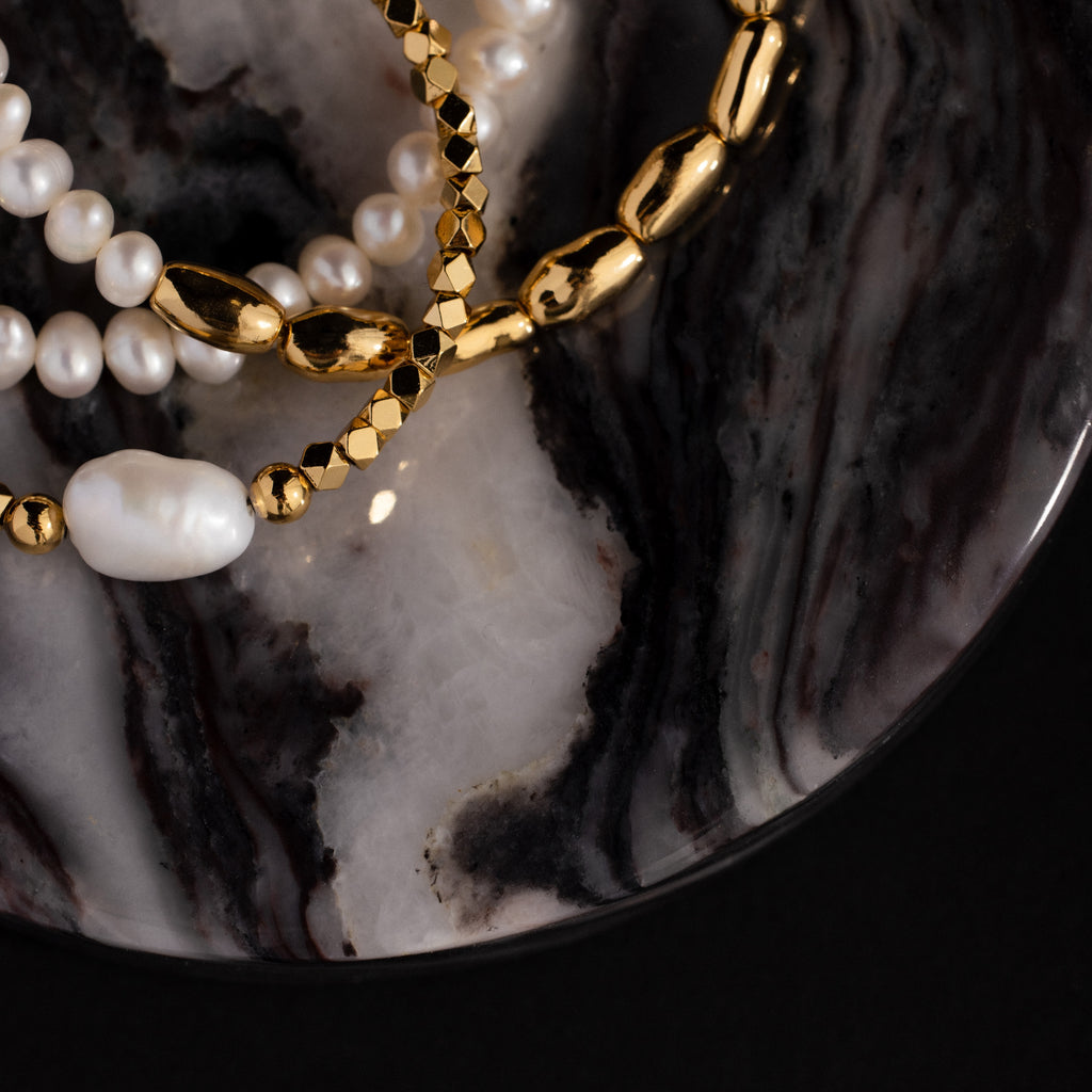 Gold and pearl bracelets arranged on an Onyx Marble Jewelry Dish with elegant black, white, and grey swirls.
