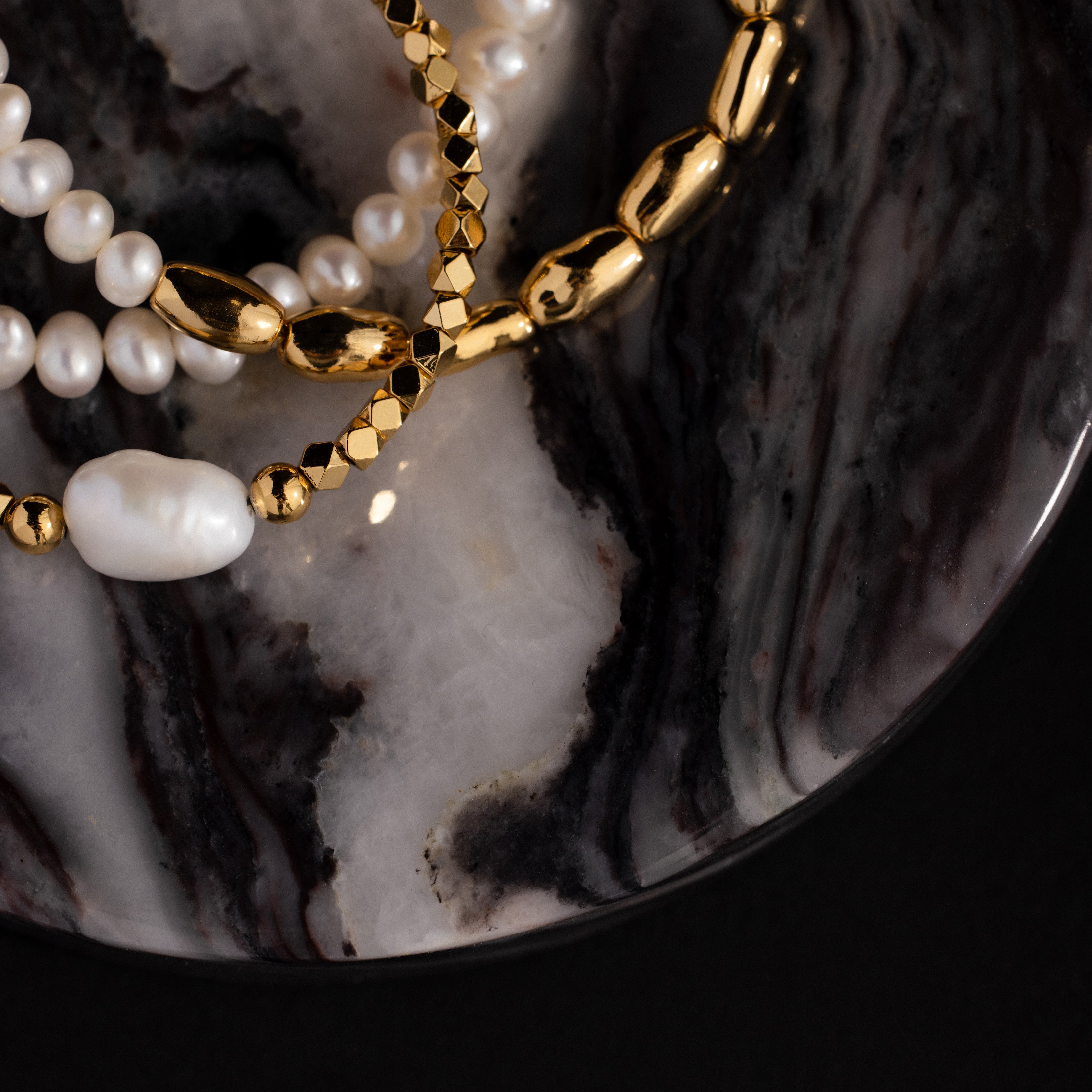 Gold and pearl bracelets arranged on an Onyx Marble Jewelry Dish with elegant black, white, and grey swirls.