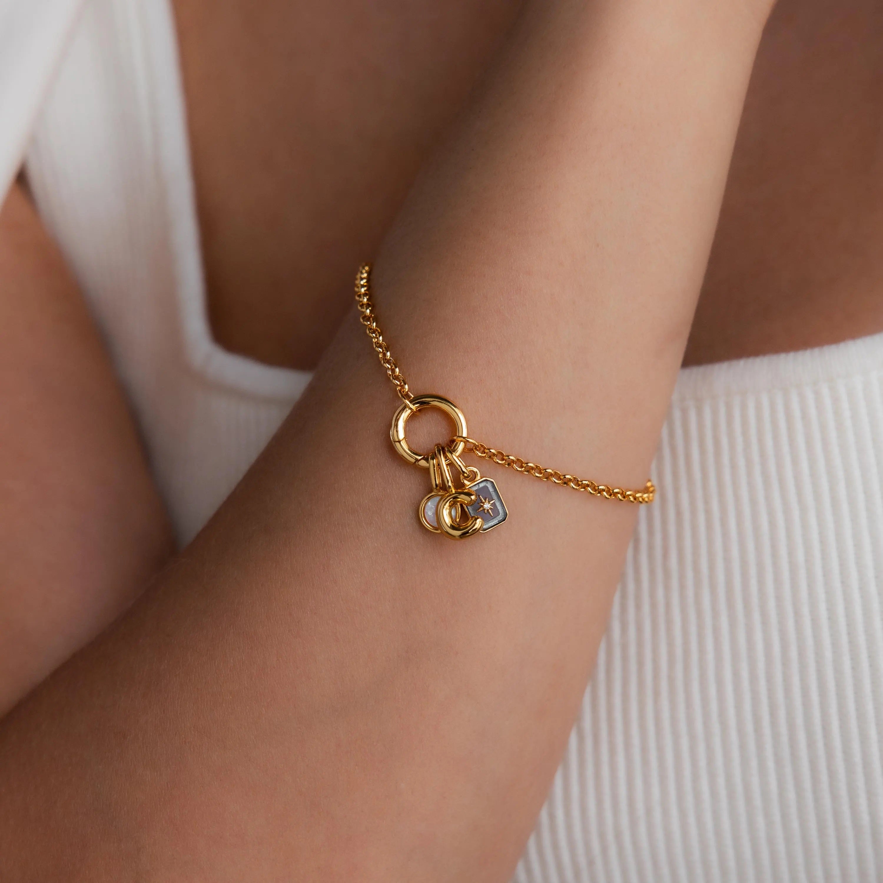 Model wearing a dainty gold rolo charm bracelet with an opal signet charm, bubble letter "C" charm, and aquamarine north star charm.