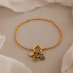 Dainty gold rolo charm bracelet with an opal signet charm, bubble letter "C" charm, and aquamarine north star charm displayed on a neutral background.