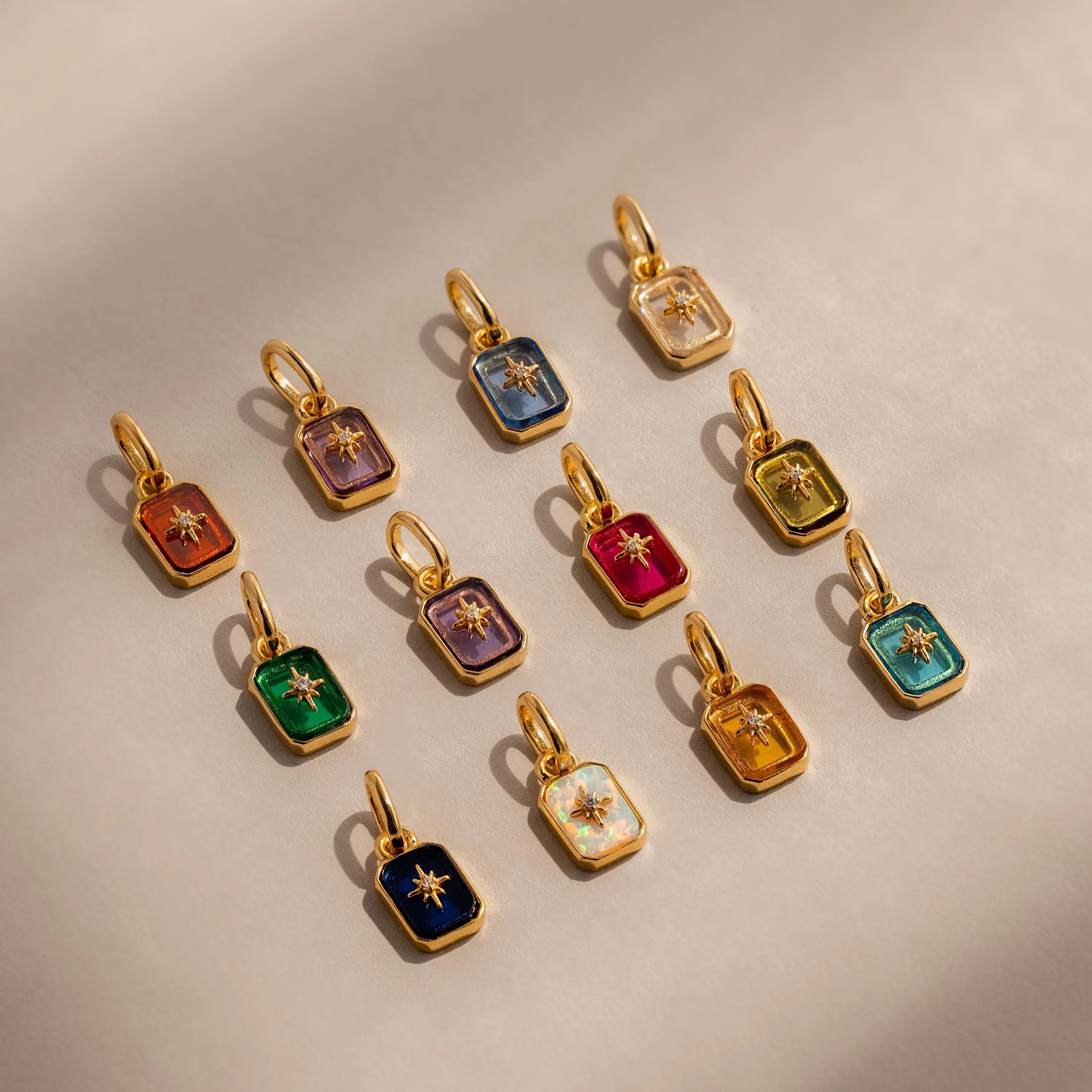 Flat lay of 12 Gold North Star Birthstone Charms in an array of vibrant colors.