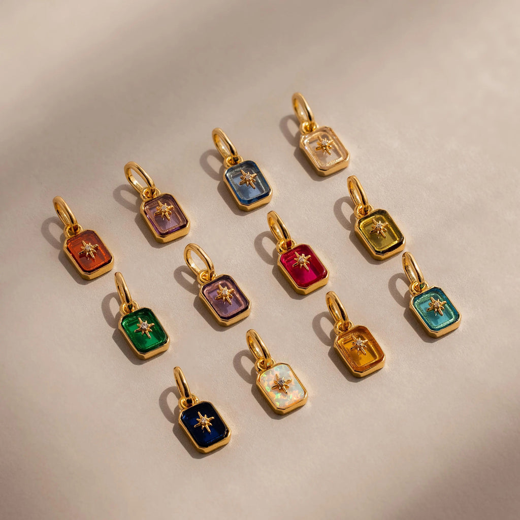 Flat lay of 12 Gold North Star Birthstone Charms in an array of vibrant colors.