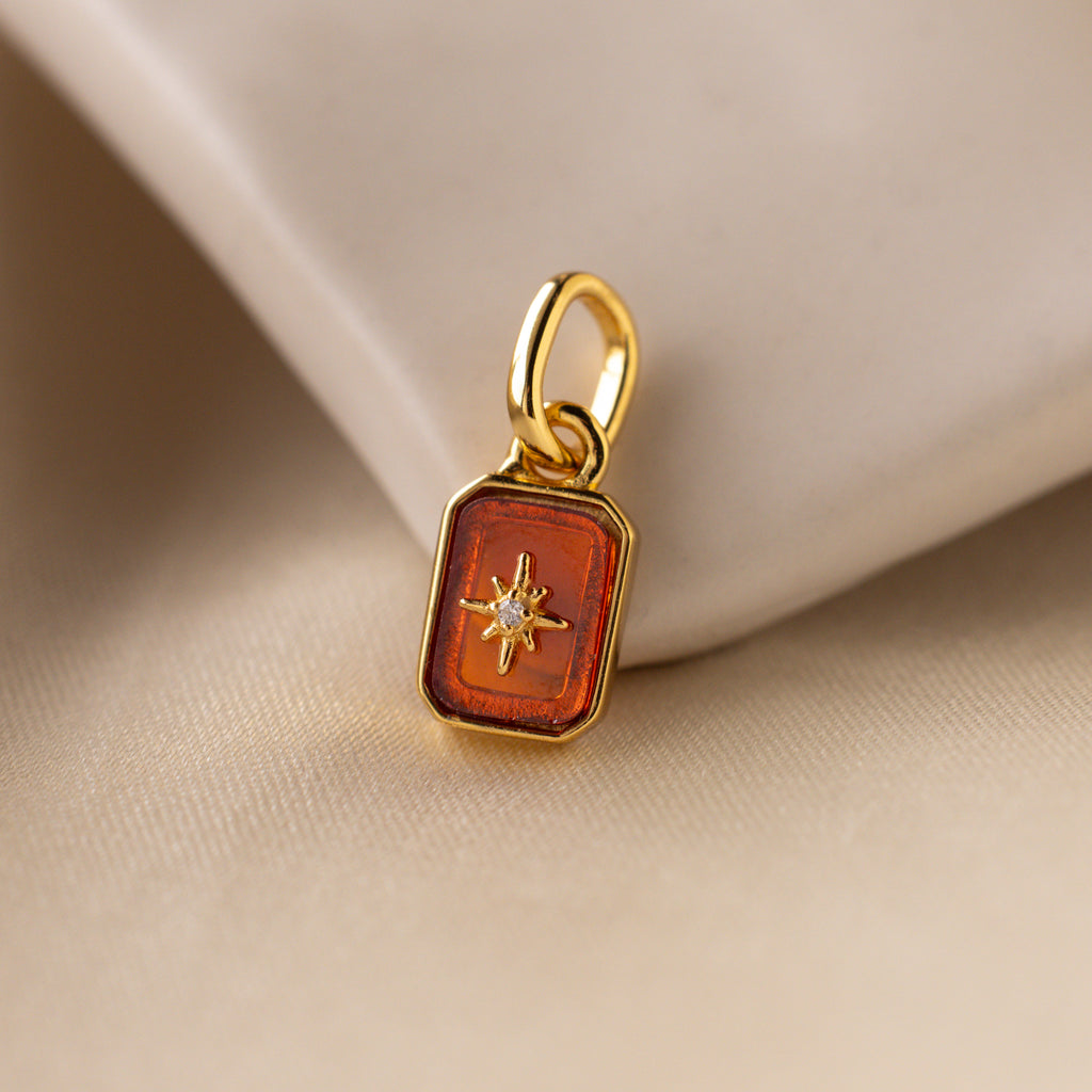 Up close of a red garnet north star charm with a delicate pavé diamond in the center.