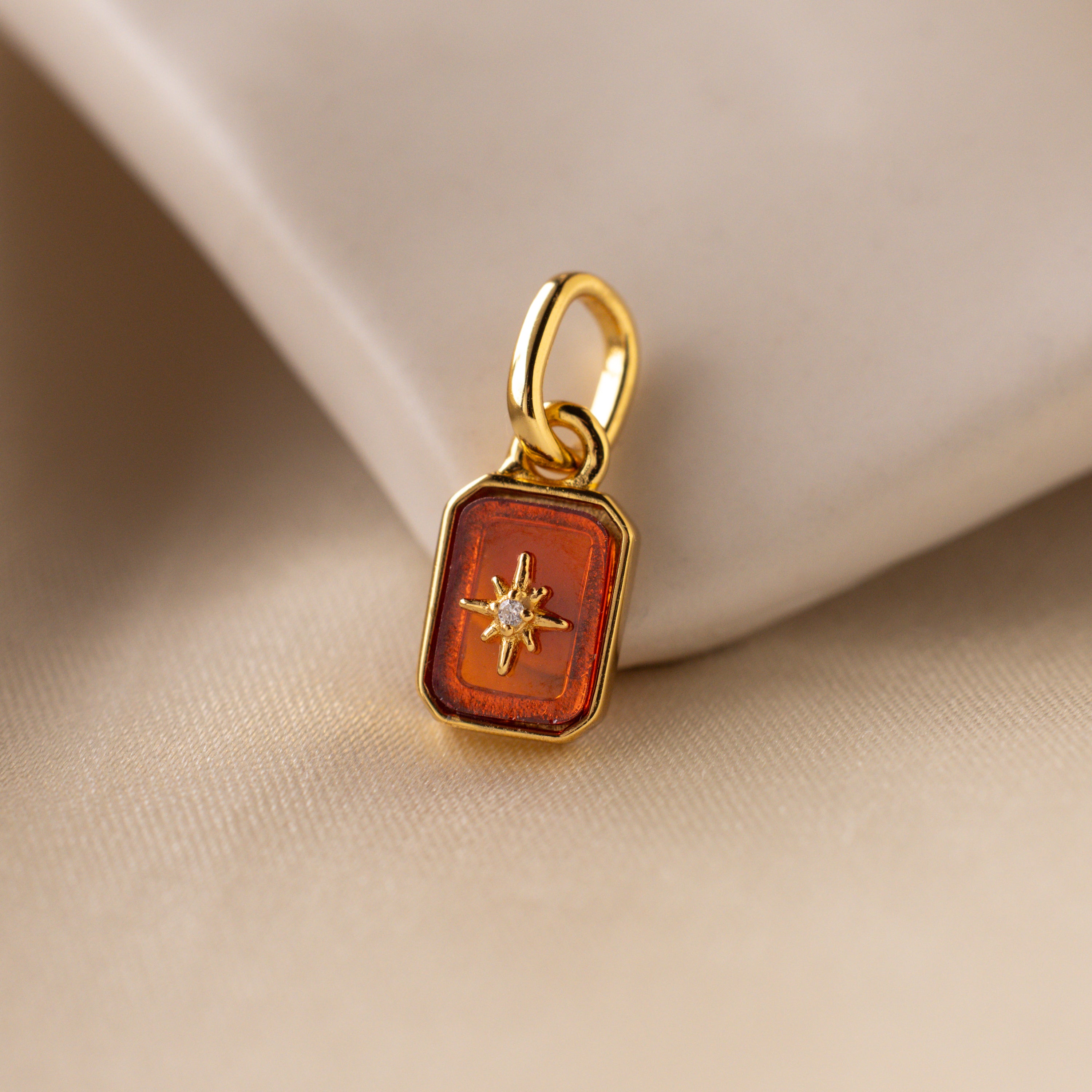 Up close of a red garnet north star charm with a delicate pavé diamond in the center.