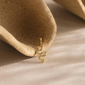 Single gold viper charm resting against the hollow curve of a textured, clay-toned ceramic prop.