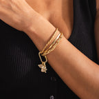 A gold Pavé Viper Charm dangles from a chunky paperclip chain bracelet, worn alongside two additional gold bracelets on a model’s wrist. The charm is paired with a pavé evil eye charm for a layered, statement look.