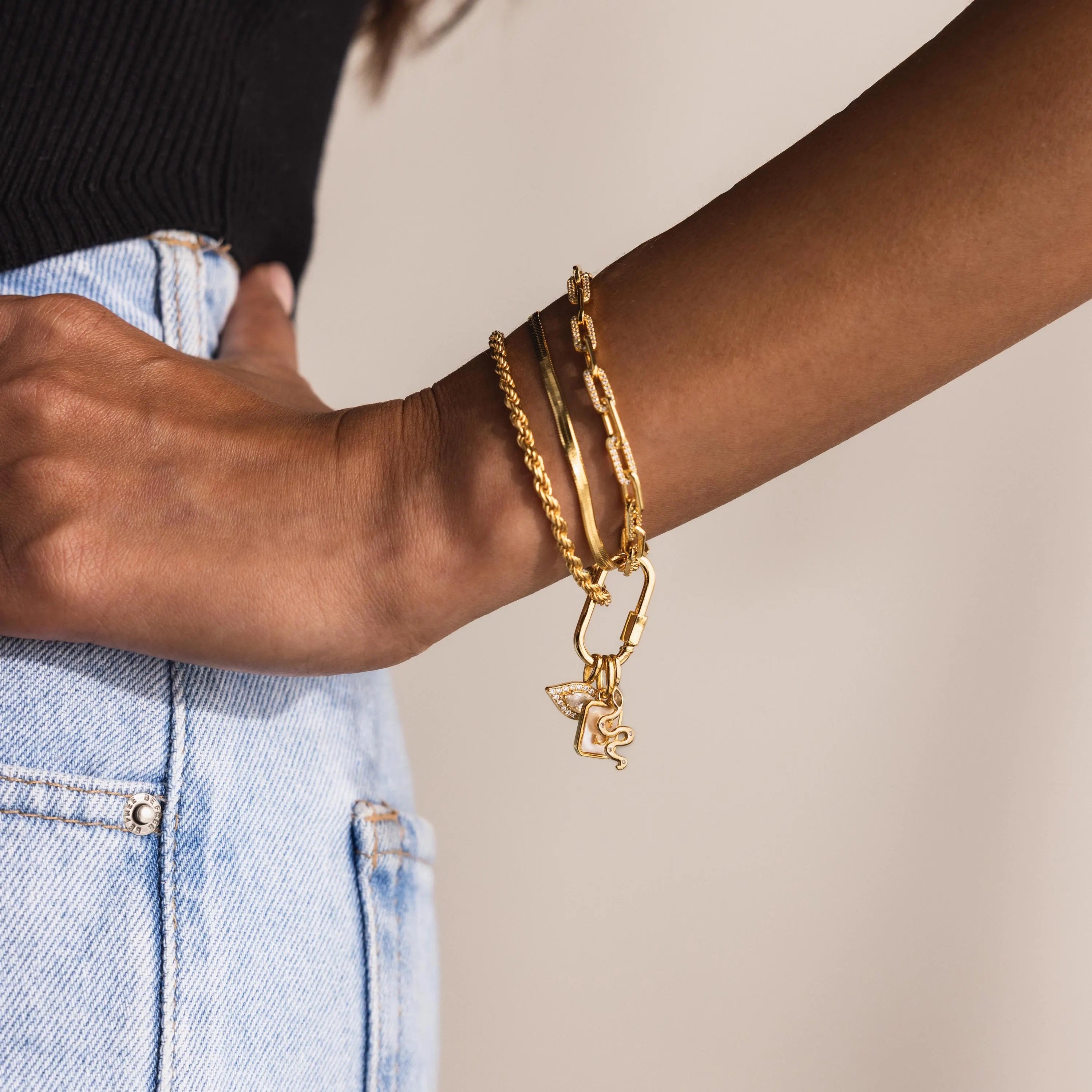 Close-up of a model’s wrist wearing a layered gold bracelet stack featuring the Pavé Viper Charm and additional symbolic charms