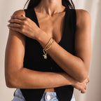 Model with arms crossed wearing a sleeveless black top. Her wrist showcases a gold bracelet stack featuring the Pavé Viper Charm along with others, standing out against her skin and minimalist attire.