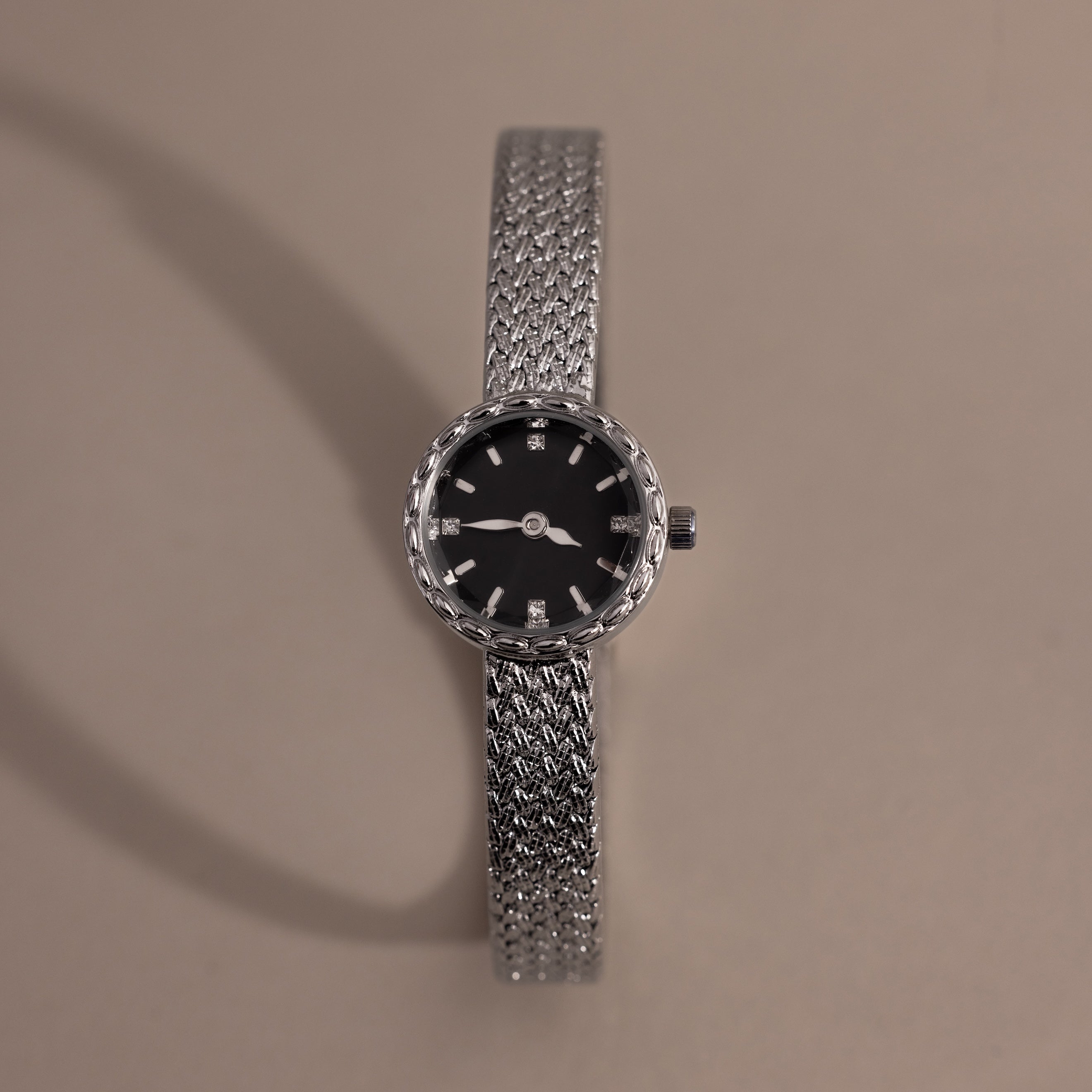 Silver braided timepiece with a black face centered on a neutral background.