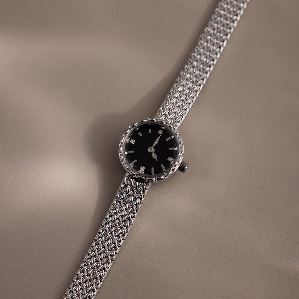 Flat-lay angle of the silver watch casting a shadow on beige surface.