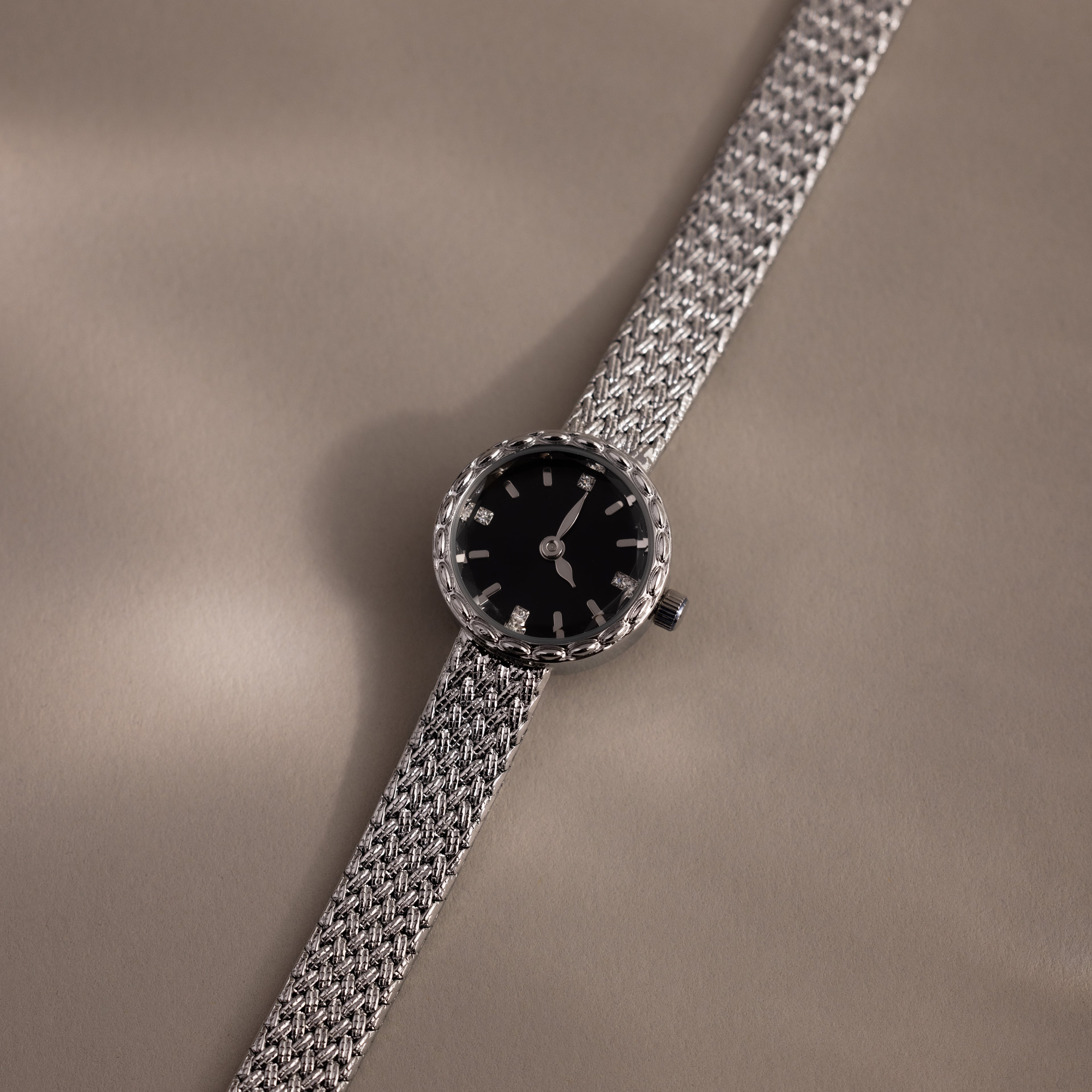 Flat-lay angle of the silver watch casting a shadow on beige surface.