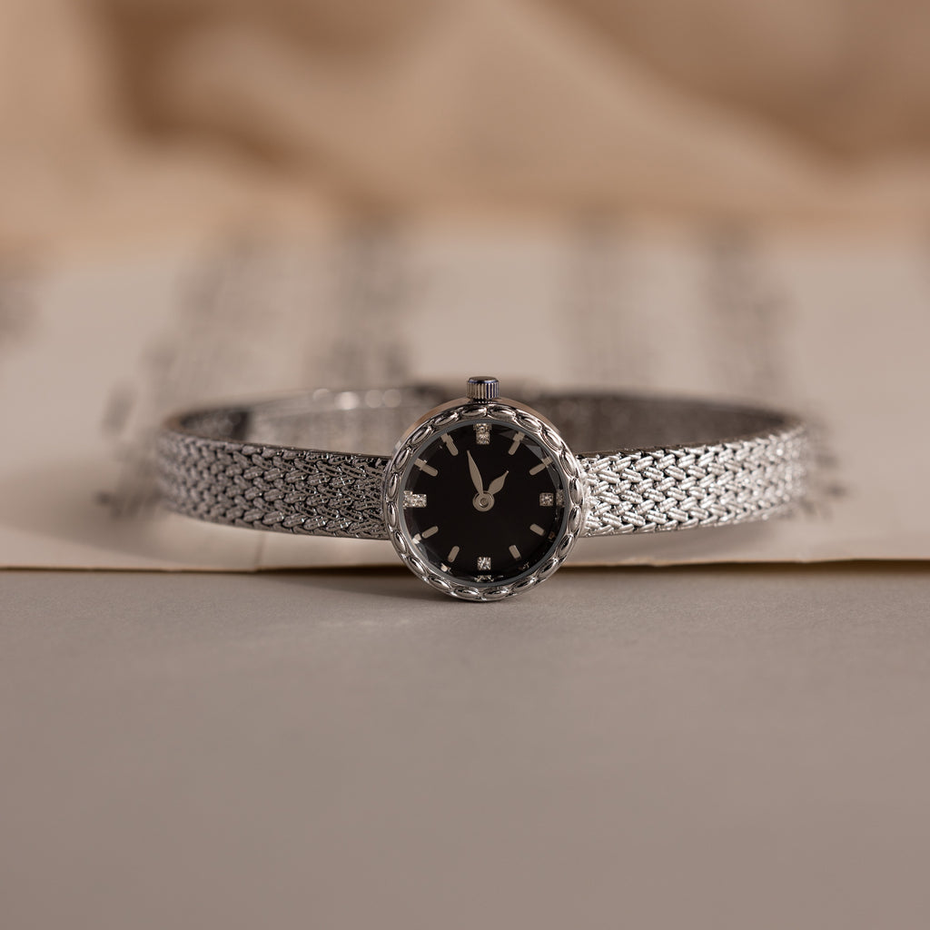 Side angle of the silver watch resting on paper, showcasing its polished finish.