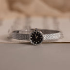 Side angle of the silver watch resting on paper, showcasing its polished finish.