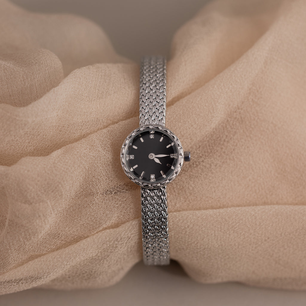 Silver timepiece displayed over soft beige fabric for a delicate look.