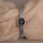 Silver timepiece displayed over soft beige fabric for a delicate look.