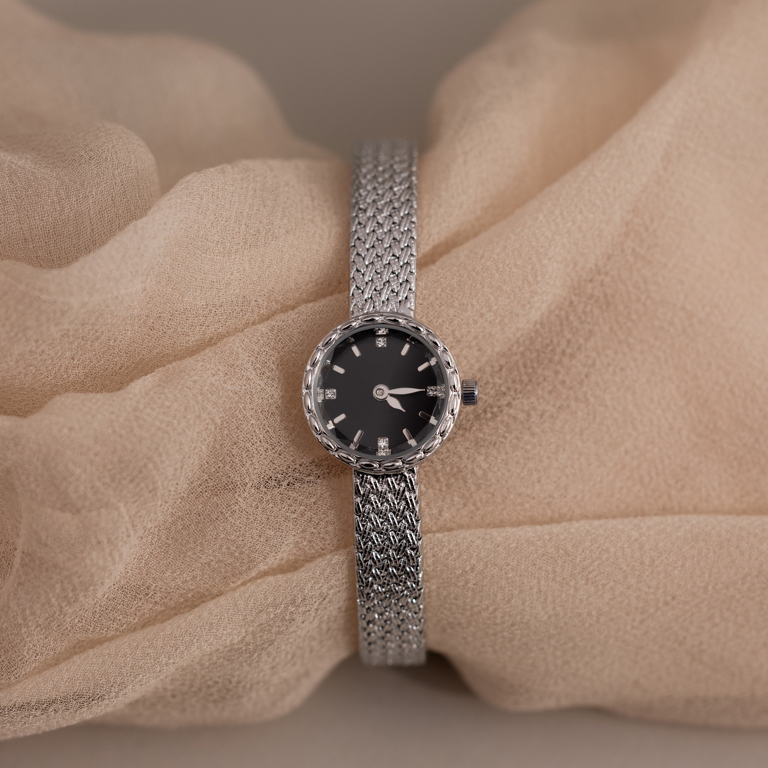 Silver timepiece displayed over soft beige fabric for a delicate look.