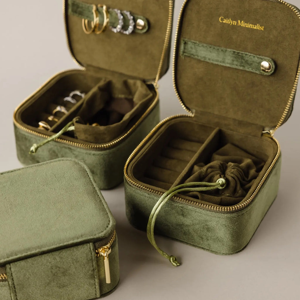 Three Green Velvet Jewelry Boxes sit on a beige surface—two open displaying rings and earrings, one closed. These elegant boxes are perfect for jewelry storage or as a travel accessory.