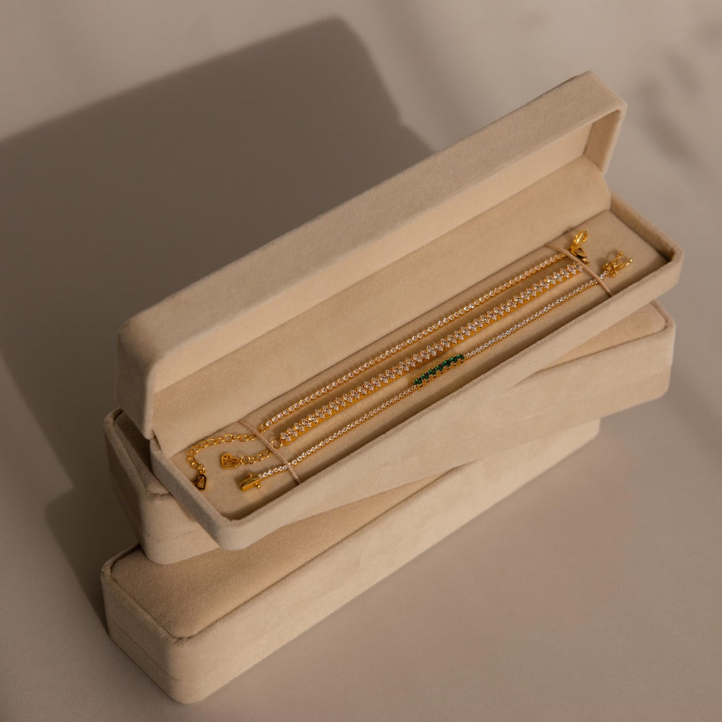 A Bracelet Travel Case in beige velvet holds a gold chain bracelet, displayed on a neutral surface with soft shadows.