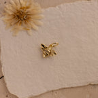 The Honeybee Charm in 18K Gold is displayed on textured white paper with a dried flower accent—an ideal gift for nature jewelry lovers.